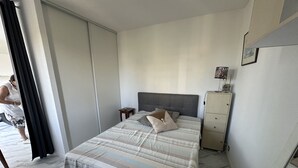 Une chambre à coucher avec un lit, une table de chevet, une commode et une fenêtre avec des rideaux.