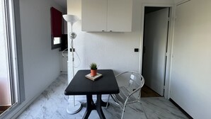 Une petite pièce moderne, avec une table noire, une chaise transparente, une plante en pot et un meuble blanc.