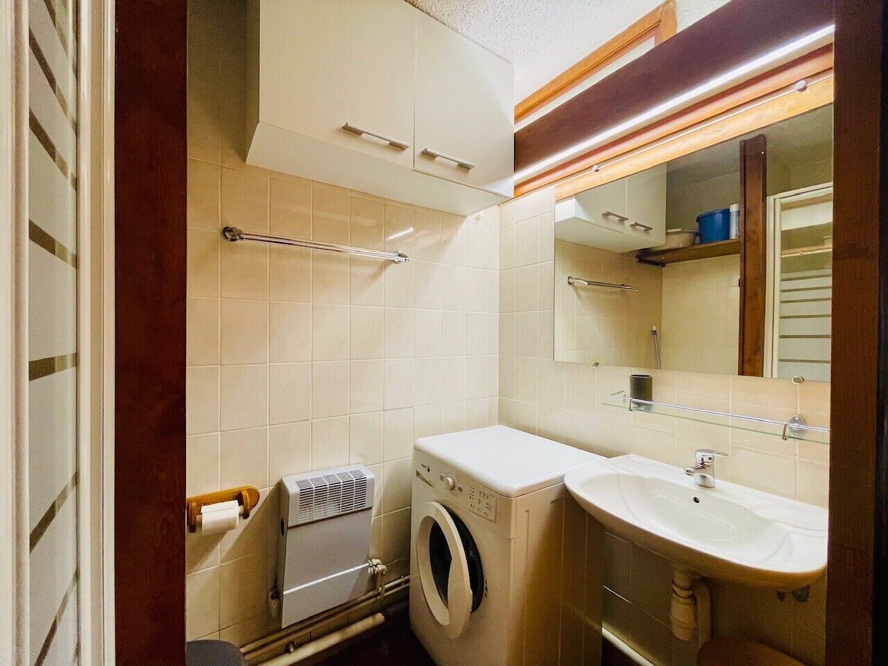 A compact bathroom with a washing machine, a sink, and a mirror.