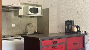 Cozinha compacta com micro-ondas, chaleira e cafeteira em bancada.