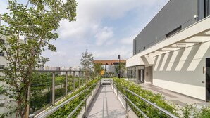 Un bâtiment moderne doté d’une façade en verre, d’un chemin bordé de rampes métalliques et d’une végétation luxuriante de chaque côté.