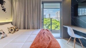 Une chambre d’hôtel moderne, dotée d’un grand lit, d’un bureau et offrant une vue sur la ville grâce à une grande fenêtre.