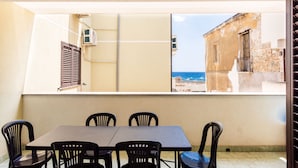Un balcone con tavolo e sedie, affacciato su un edificio con vista sul mare.