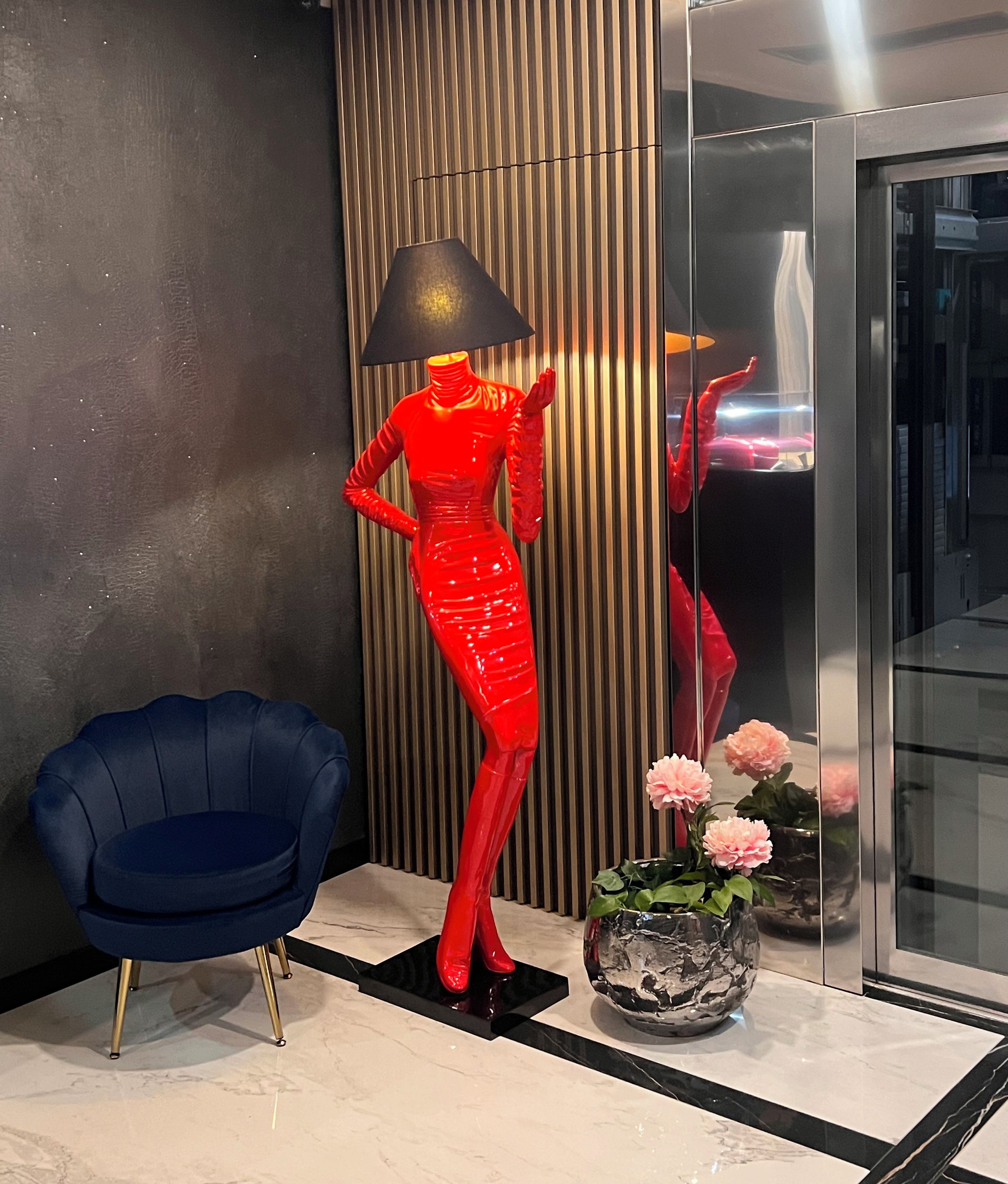 Ein modernes Interieur mit einem blauen Stuhl, einer roten Skulptur und einer Vase mit Blumen.