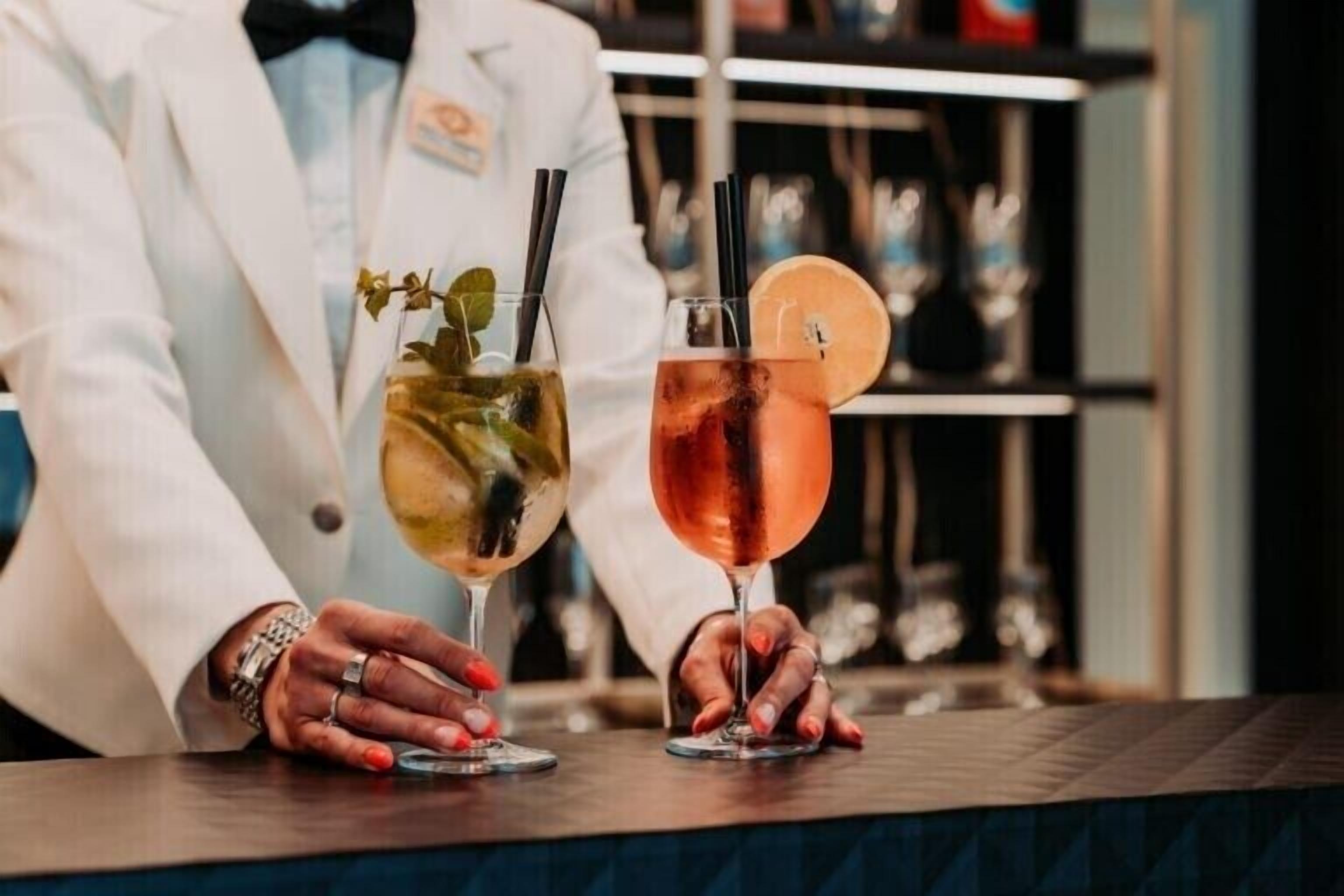 A bartender holding two cocktails with straws and garnishes.