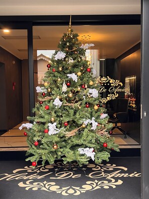 A Christmas tree with ornaments and lights in a hotel lobby. - HOTEL DE AMICIS  (Moglia)