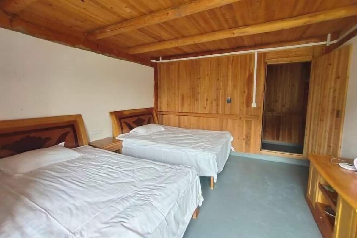 A room with two single beds, wooden ceiling beams, a wardrobe, and a small wooden table.