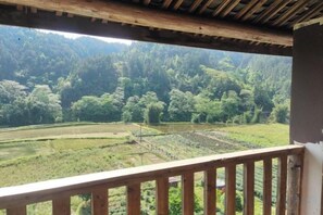 A view from a balcony with a wooden railing, overlooking a terraced field and forested hills. - Sanjiang Panjin Farmhouse (Sanjiang)