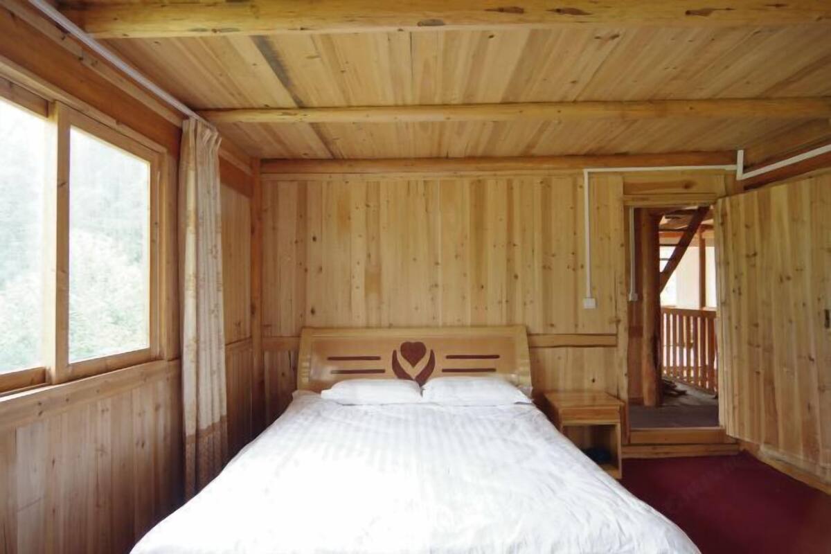 A wooden cabin room with a bed, a small table, and a window.