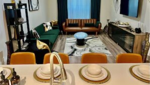 A living room with a sofa, a dining table set with plates, and a TV mounted on the wall. -  New! Luxury Midtown Escape (Houston)