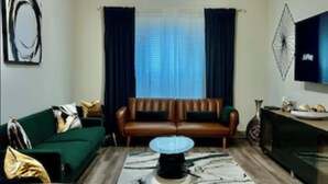 A living room with a brown leather sofa, a green couch, a coffee table, and a TV on a stand. -  New! Luxury Midtown Escape (Houston)