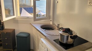 A compact kitchen with a built-in washer and dryer, a window with a view of the sea, and wooden cabinets. - Le rivage d'hélène - Apartment Sea view - 2 pers - 1 bedroom - All comfort (Ault)