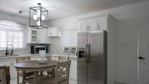 A modern kitchen with white cabinetry, a stainless steel refrigerator, a dining table with chairs, and a pendant light. - Island Dreams Villa at Legacy Townhouse (Montego Bay)