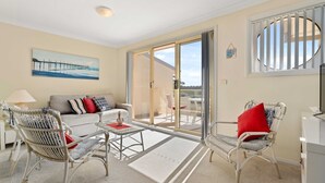 A living room with a sofa, two wicker chairs, a glass coffee table, and a painting of a pier. - Pier 8 by Experience Jervis Bay (Huskisson)