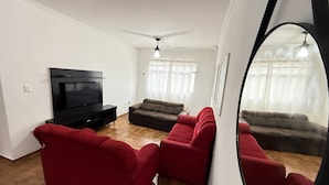 Una sala de estar con un televisor de pantalla plana, dos sofás, un ventilador de techo y un espejo grande.