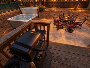 Un patio trasero con jacuzzi, una parrilla y un comedor con sillas y una mesa.