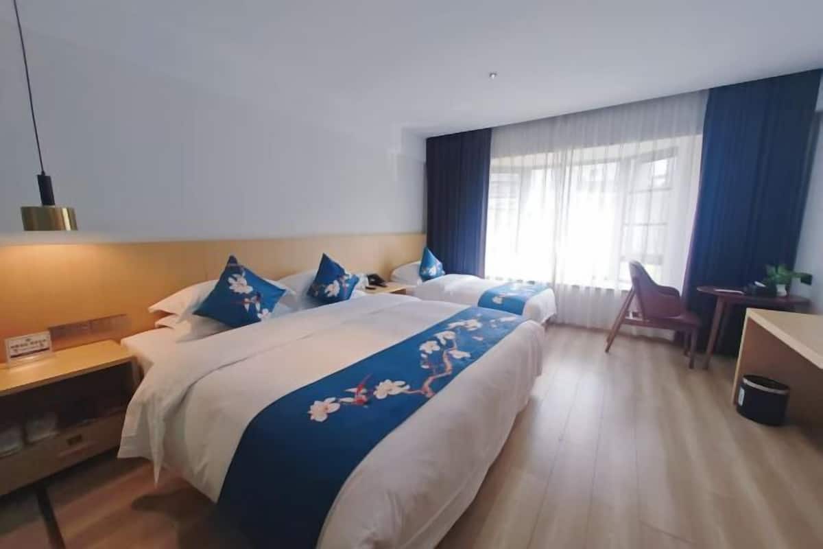 A hotel room with two beds, a desk, a chair, a nightstand, and a window with curtains.