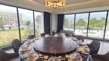 A conference room with a round table set for a meeting, large windows with a view of the city, and a modern chandelier.