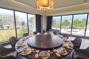 Een vergaderzaal met een ronde tafel, klaar voor een vergadering, grote ramen met uitzicht op de stad en een moderne kroonluchter.