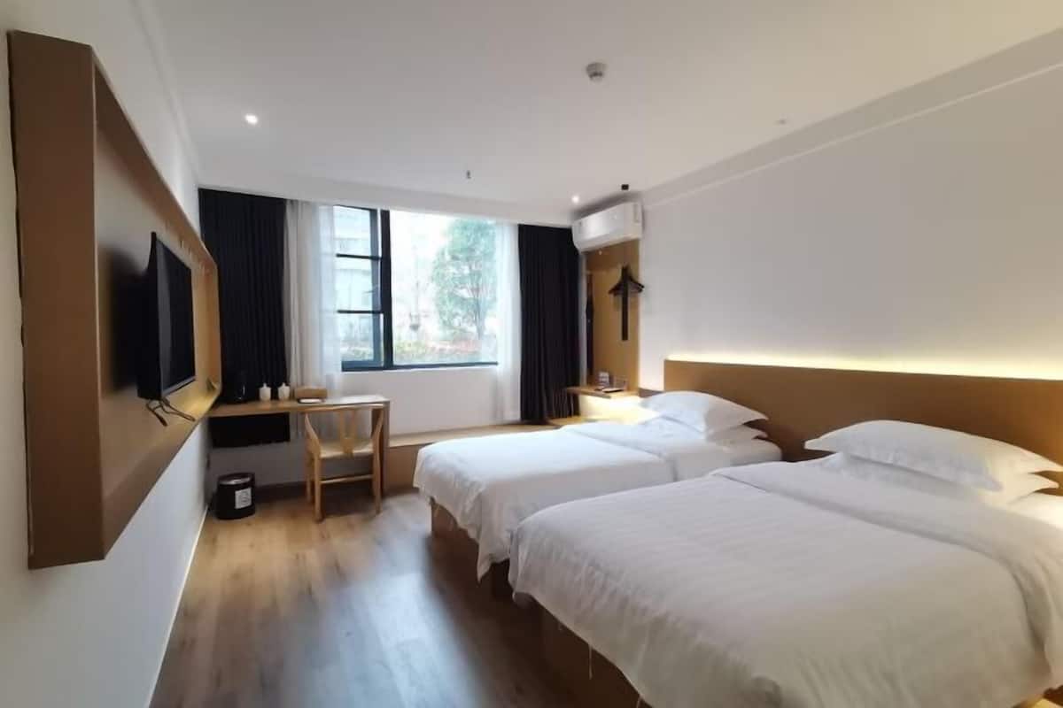A hotel room with two beds, a desk, a chair, and a TV.