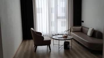 Una sala de estar moderna con un sofá, un sillón, una mesita redonda y un ventanal con cortinas de encaje.