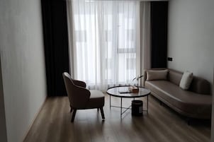 Una sala de estar moderna con un sofá, un sillón, una mesita redonda y un ventanal con cortinas de encaje.