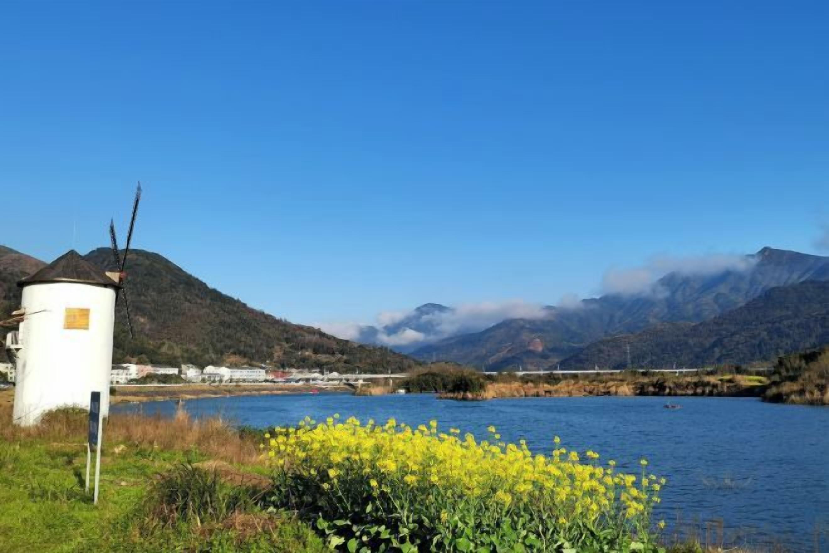 A white cylindrical structure near a body of water with mountains in the background.
