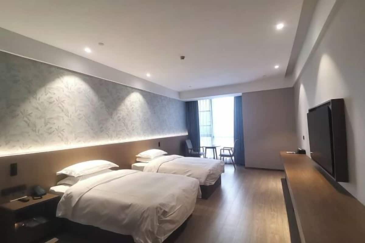A hotel room with two beds, a flat-screen TV, a large window, and a seating area with chairs.