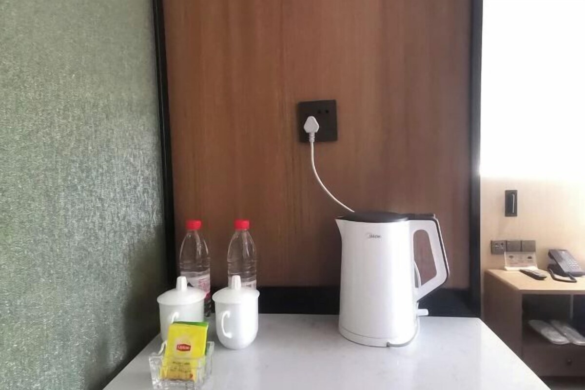 A kitchenette with a coffee maker, a kettle, a bottle of water, a jug, and a packet of sugar.