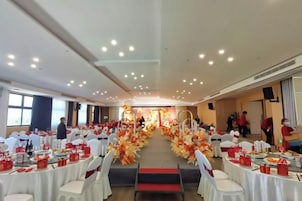 Un salón de banquetes con mesas redondas, sillas y un pasillo central adornado con arreglos florales.