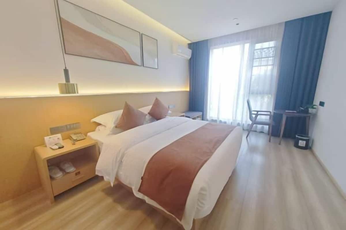 A hotel room with a bed, bedside table, lamp, and a desk with a chair.