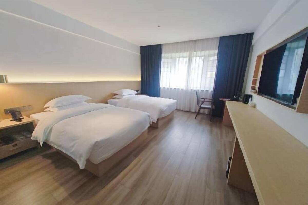 A hotel room with two beds, a desk, a chair, and a TV.