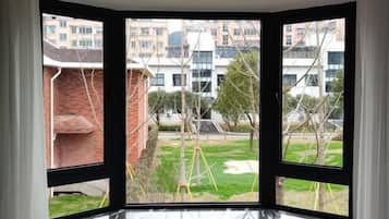 A corner room with a view of a residential area, including buildings and a grassy field.