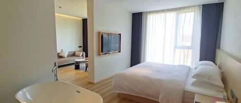 A modern hotel room with a large bed, a bathtub, a sofa, and a TV.