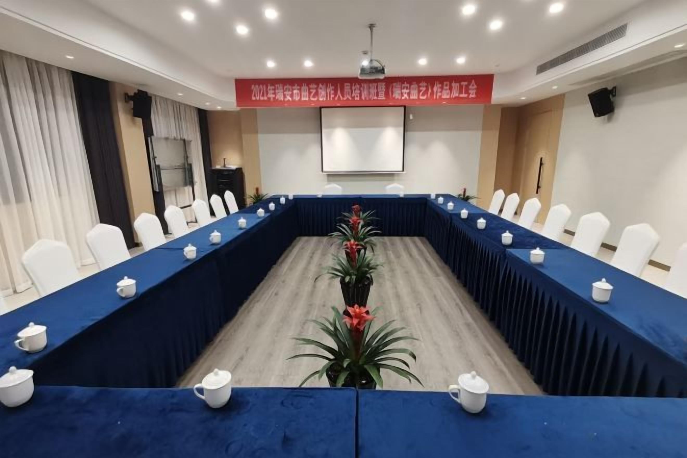 A conference room with a long table, white chairs, and a blue tablecloth.