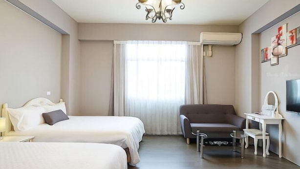 Een hotelkamer met twee bedden, een bureau, een stoel, een televisie en een raam met gordijnen.