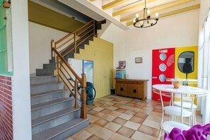 Un escalier menant à un deuxième étage, un coin repas avec une table et des chaises blanches, et un mur rouge orné de motifs circulaires.