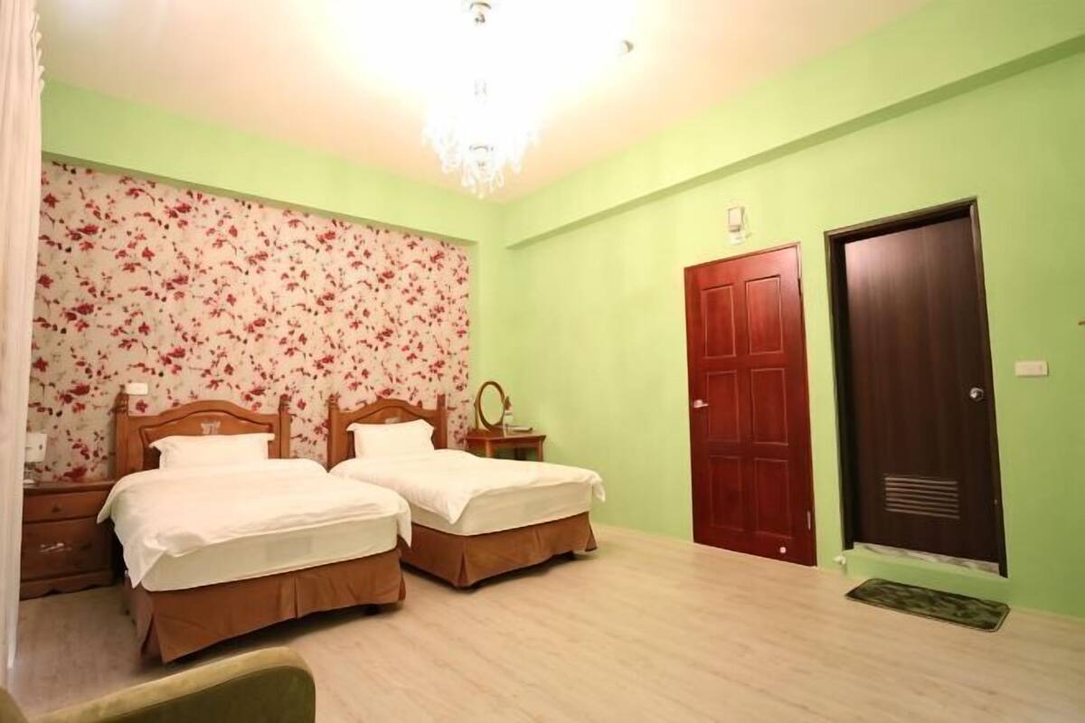 A room with two beds, a wooden door, and a chandelier.