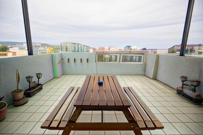 Une terrasse sur le toit, avec une table et des chaises en bois, des plantes en pot et une vue sur le paysage urbain.