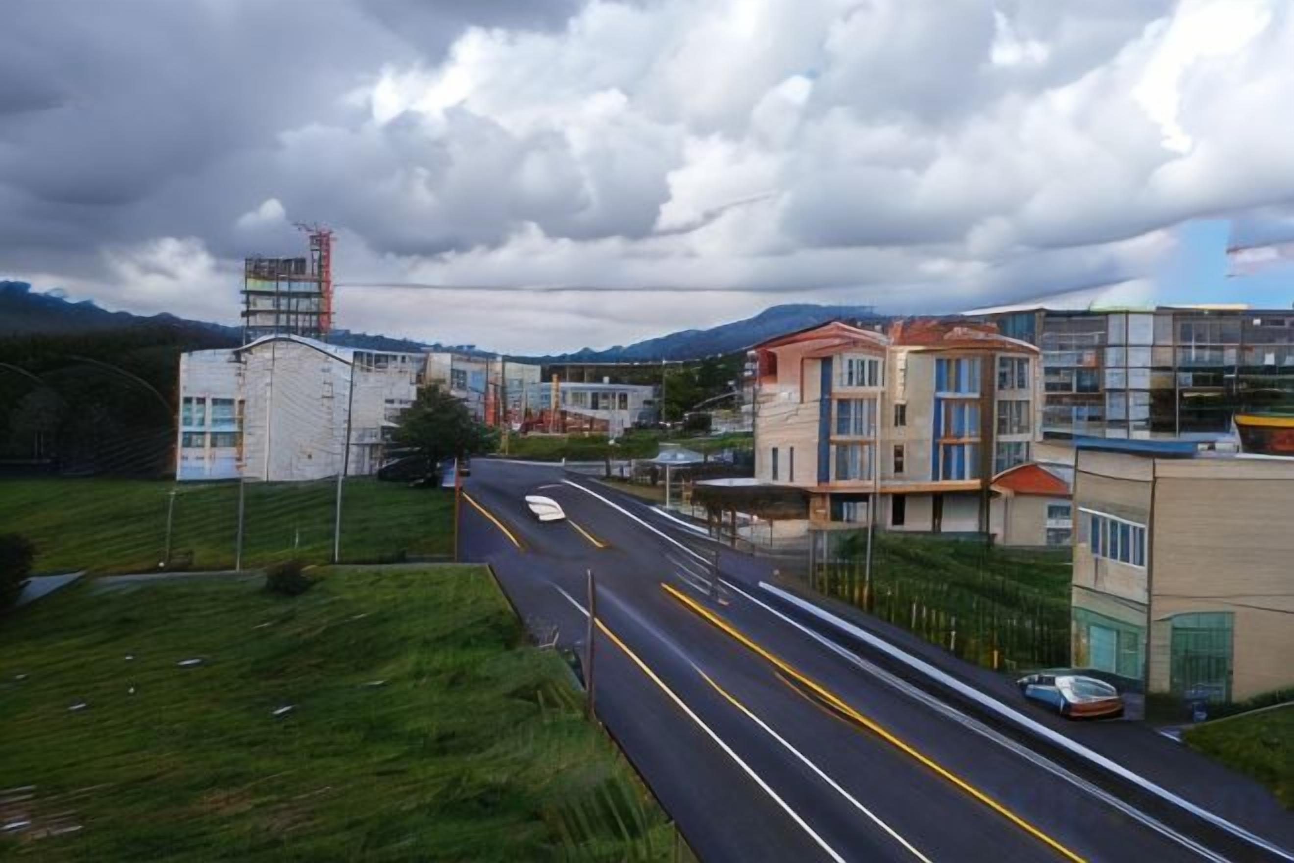 A road with buildings on the right, a clear sky, and a distant mountain range.