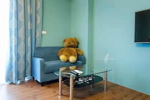 Ein Zimmer mit einem blauen Sofa, einem Glastisch und einem großen Teddybären.