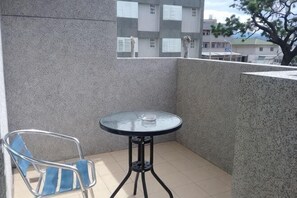 A balcony with a round glass table and a chair, a tiled floor, and a view of buildings and a tree. - Slow Travel Taitung B&B (Taitung)