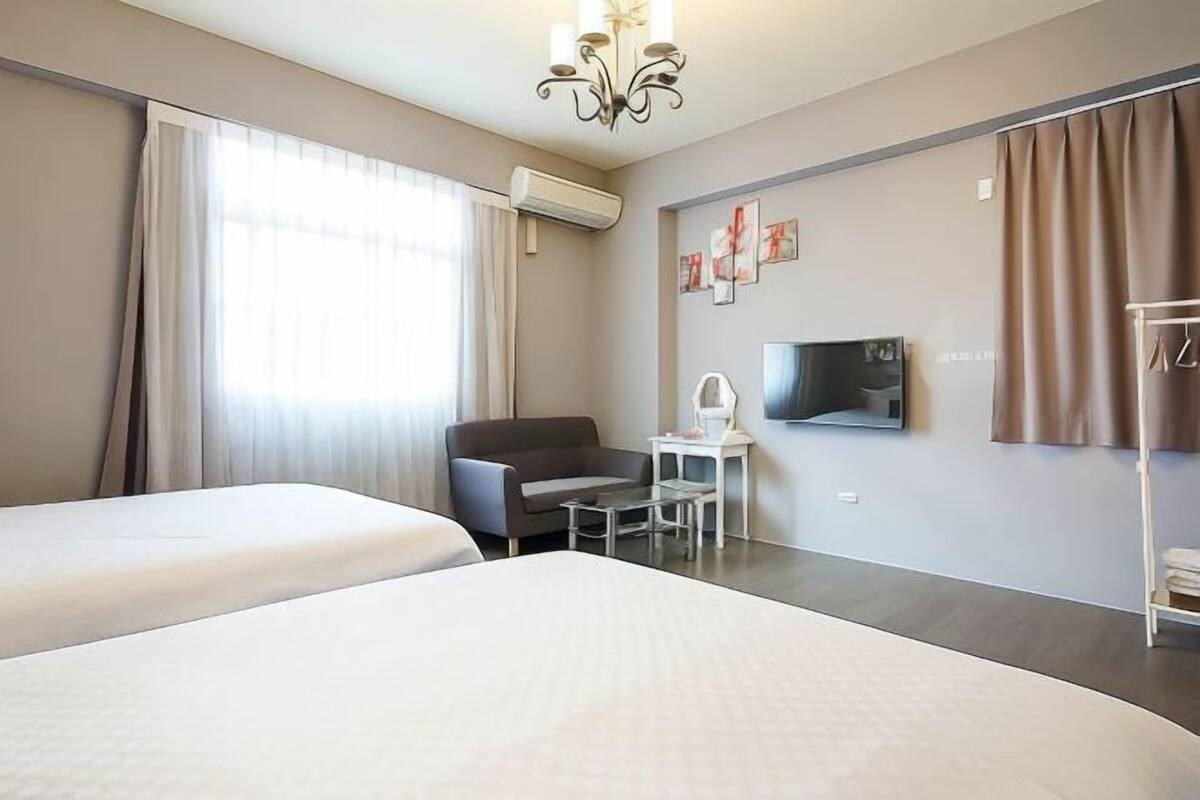 A hotel room with two beds, a desk, a chair, a TV, and a wardrobe.