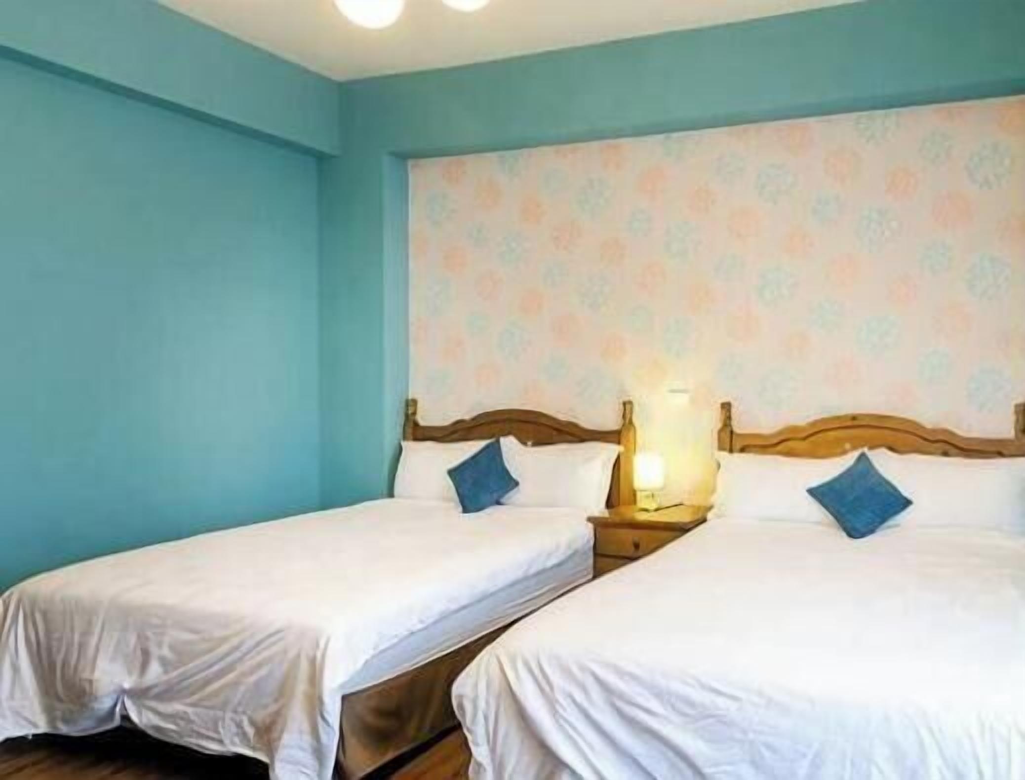 A room with two single beds, a wooden headboard, a nightstand with a lamp, and a patterned wall.
