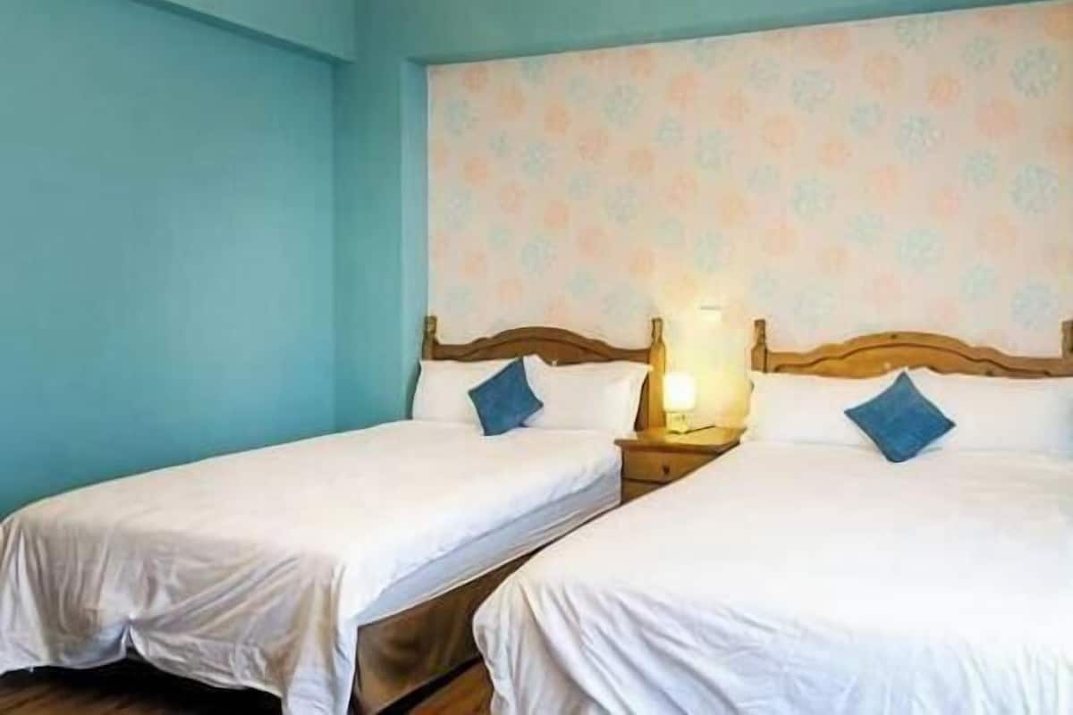 A room with two single beds, a wooden headboard, a nightstand with a lamp, and a patterned wall.