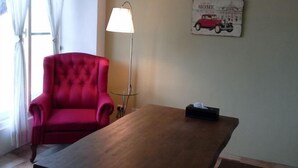 Een kamer met een rode fauteuil, een houten tafel, een vloerlamp en een decoratie aan de muur.