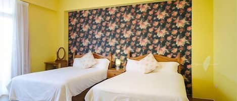 Une chambre d’hôtel avec deux lits, une tête de lit à motifs floraux, un lustre et une table de chevet avec une lampe.