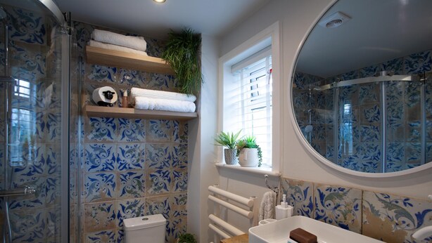 Un baño con ducha, inodoro y lavamanos. Hay estantes con toallas y plantas.
