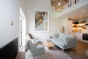 Una sala de estar moderna con un sofá gris claro, una mesa de centro de madera y un espejo grande con estampado floral.