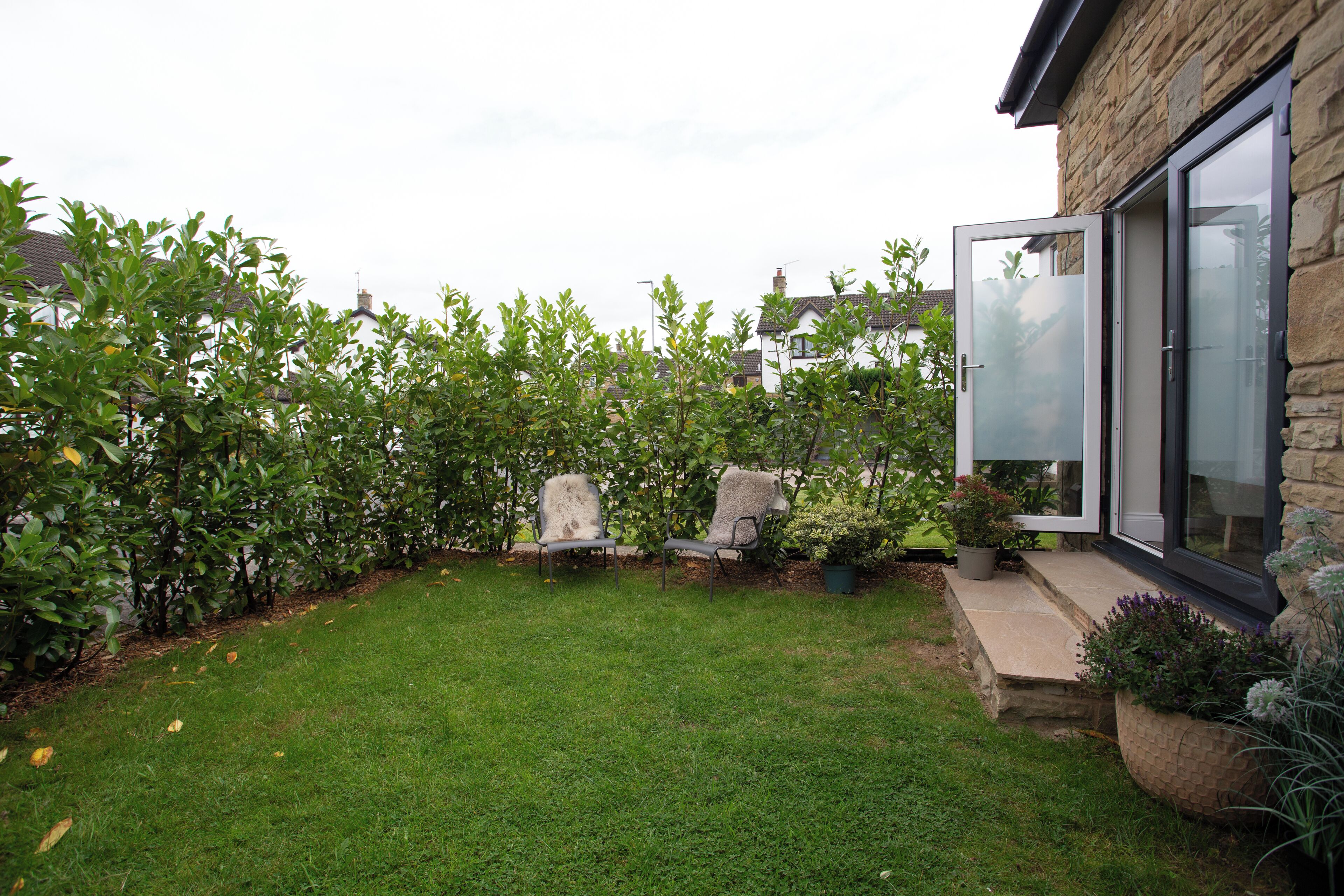 A well-maintained garden with a lawn, two chairs, and a stone wall.